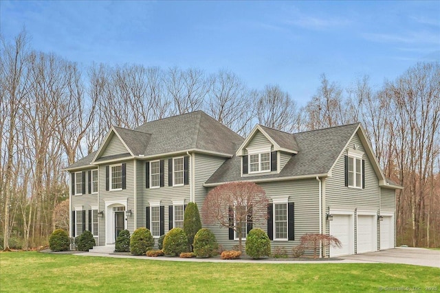colonial house with a garage, a shingled roof, a front lawn, and concrete driveway