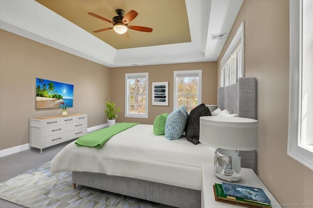 carpeted bedroom featuring a tray ceiling, visible vents, a ceiling fan, and baseboards