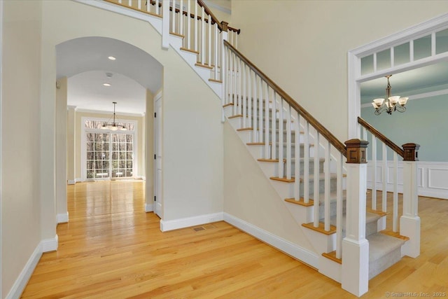 stairway featuring a chandelier, wood finished floors, arched walkways, and baseboards