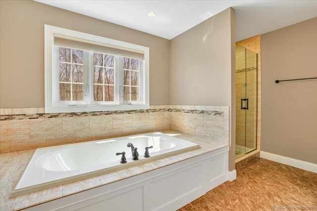bathroom with baseboards, a bath, and a stall shower
