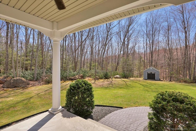 view of yard featuring an outbuilding, a wooded view, and ceiling fan