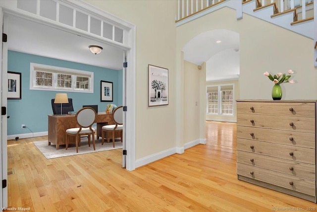 interior space featuring arched walkways, light wood-style floors, and baseboards
