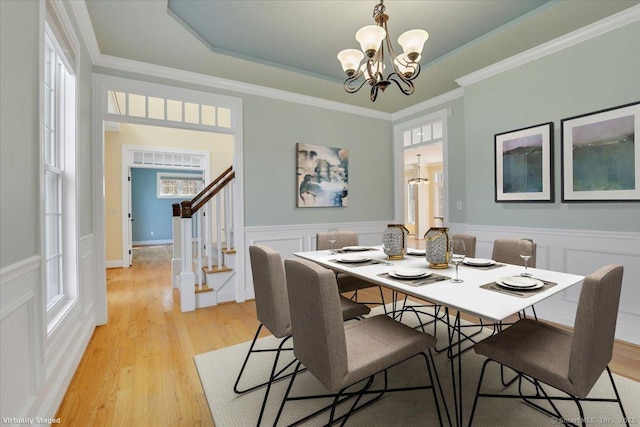 dining room with stairs, a wainscoted wall, a tray ceiling, light wood finished floors, and a notable chandelier