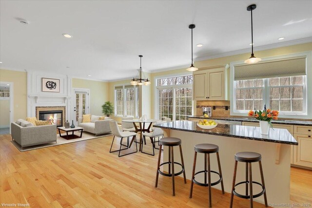 kitchen featuring light wood finished floors, a kitchen breakfast bar, open floor plan, cream cabinetry, and ornamental molding