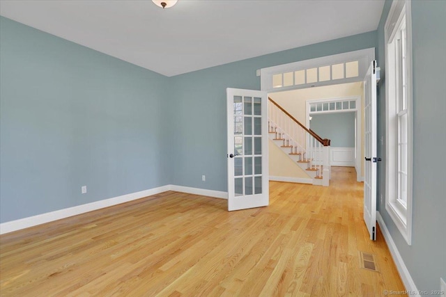 unfurnished room with french doors, light wood-style flooring, baseboards, visible vents, and stairway
