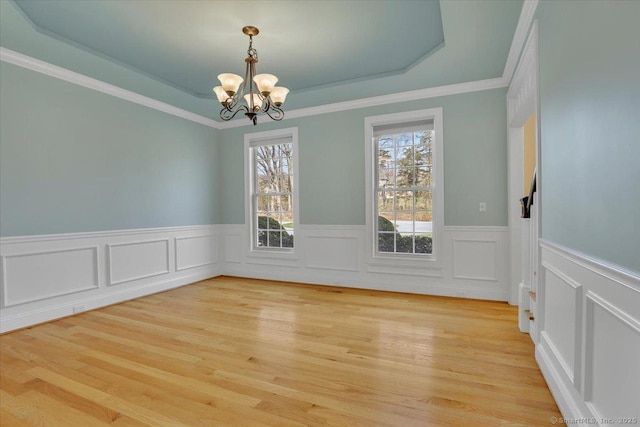 unfurnished dining area with a wainscoted wall, a tray ceiling, light wood-style floors, crown molding, and a chandelier
