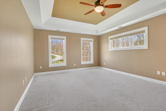 spare room featuring carpet floors, a ceiling fan, a tray ceiling, and plenty of natural light