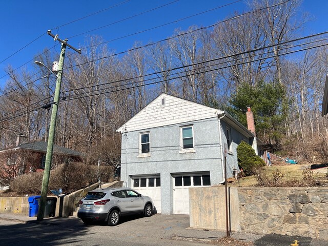 view of side of property with a chimney, driveway, stucco siding, and an attached garage