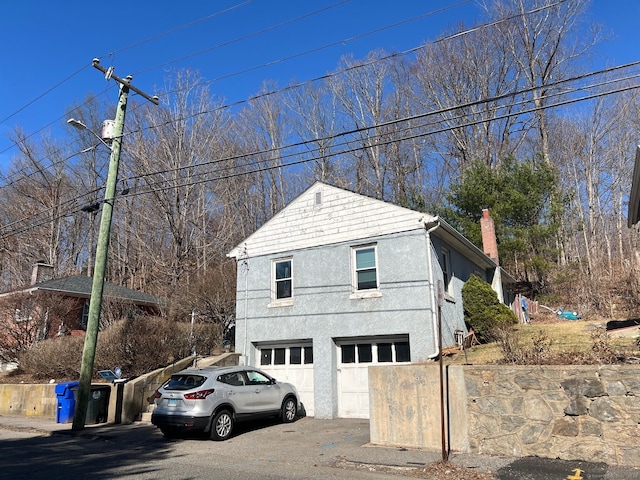 241 Harwinton Ave, Torrington, CT 06790 - view of home's exterior with stucco siding, an attached garage, driveway, and a chimney