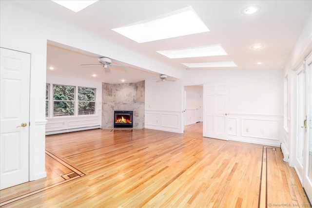 25 Jefferson Dr, New Milford, CT 06776 - unfurnished living room featuring a baseboard radiator, a decorative wall, a skylight, ceiling fan, and light wood finished floors
