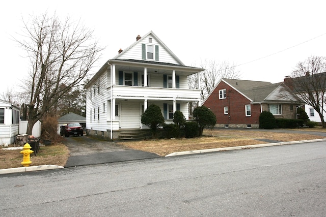view of front of home featuring aphalt driveway, a detached garage, covered porch, an outdoor structure, and a balcony