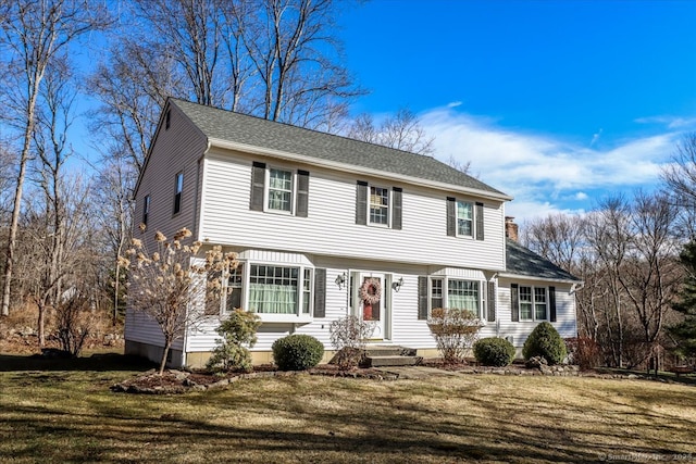 colonial home featuring a shingled roof and a front lawn