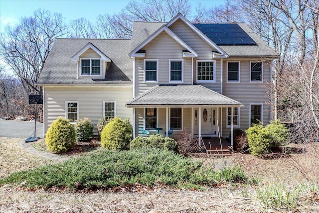view of front of house featuring roof mounted solar panels, roof with shingles, and covered porch