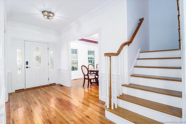 foyer entrance with stairway, ornamental molding, wainscoting, and light wood finished floors