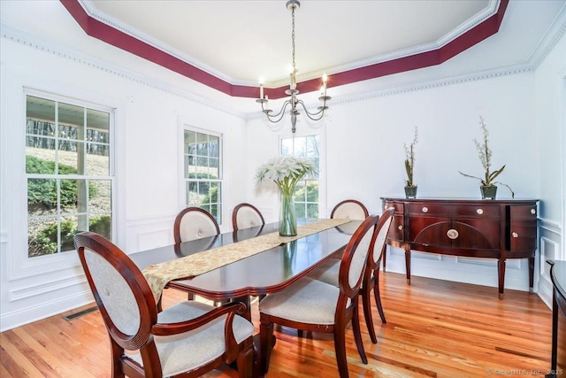 dining space featuring visible vents, ornamental molding, light wood-style floors, a notable chandelier, and a raised ceiling