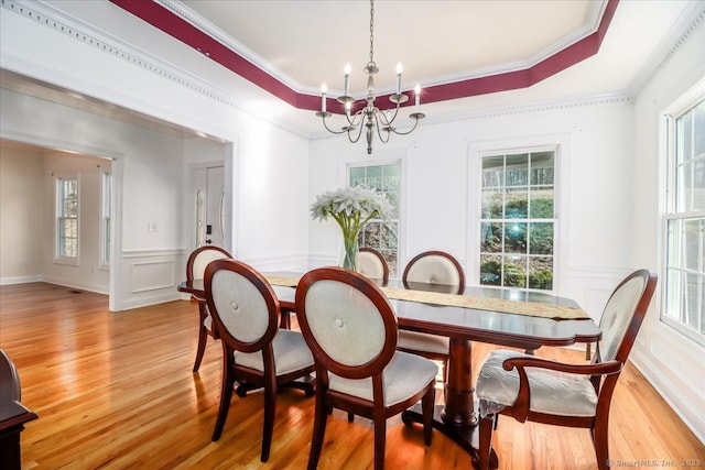 dining room with a tray ceiling, a notable chandelier, and light wood finished floors