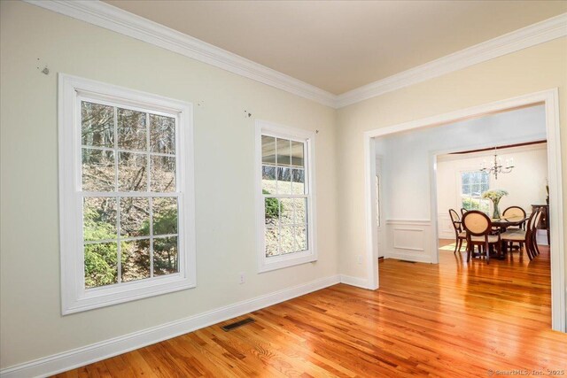 spare room with light wood-type flooring, plenty of natural light, a notable chandelier, and crown molding