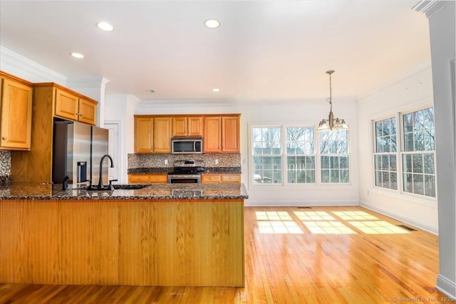 kitchen featuring a sink, dark stone countertops, tasteful backsplash, stainless steel appliances, and a peninsula