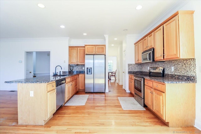 kitchen with dark stone counters, light wood-type flooring, a peninsula, stainless steel appliances, and a sink