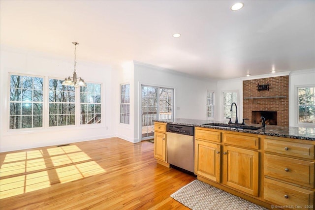 kitchen featuring light wood-type flooring, a notable chandelier, a sink, stainless steel dishwasher, and a fireplace