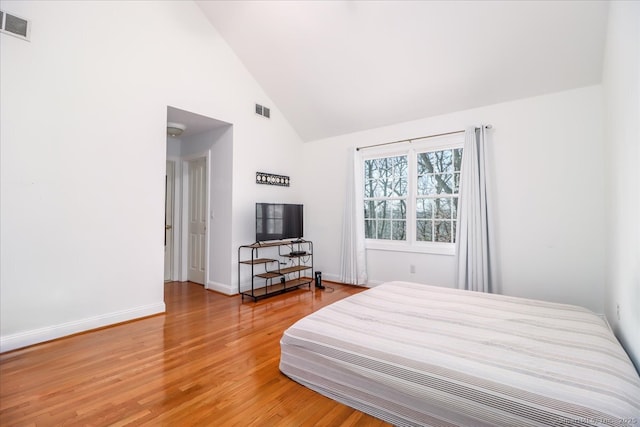 bedroom featuring visible vents, baseboards, light wood-style floors, and high vaulted ceiling