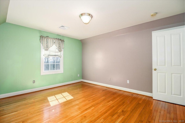 unfurnished room with visible vents, light wood-type flooring, baseboards, and vaulted ceiling