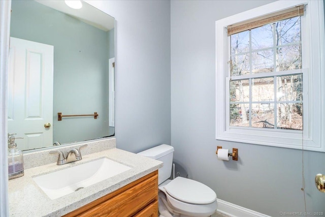 half bathroom with baseboards, plenty of natural light, toilet, and vanity