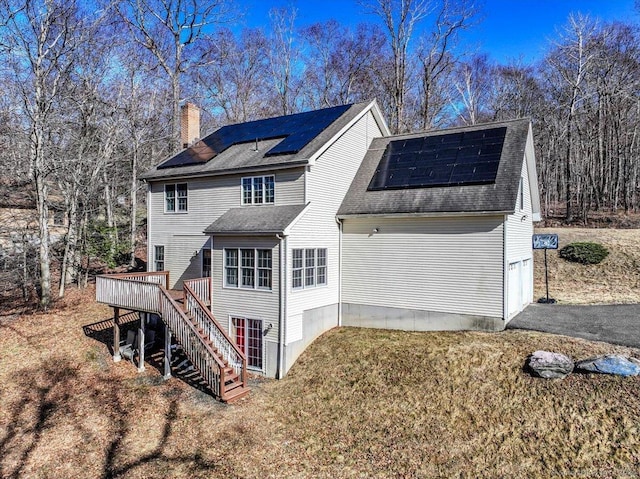 view of side of home featuring a chimney, a deck, aphalt driveway, a garage, and stairs