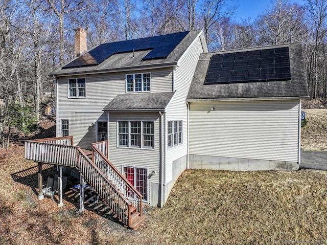 back of house with a wooden deck, stairs, roof with shingles, a lawn, and a chimney