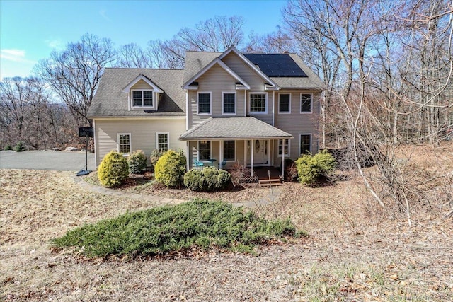 view of front facade featuring covered porch, solar panels, and a shingled roof