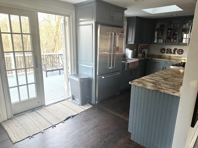 kitchen with dark wood-style floors, stone countertops, high end refrigerator, a skylight, and glass insert cabinets