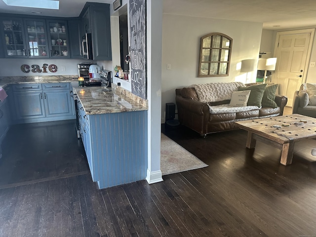 kitchen with blue cabinets, open floor plan, glass insert cabinets, appliances with stainless steel finishes, and dark wood-type flooring