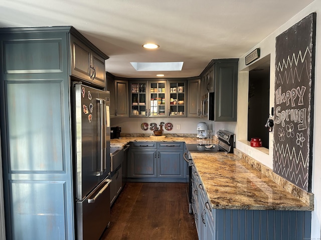 kitchen featuring recessed lighting, dark wood finished floors, a skylight, glass insert cabinets, and appliances with stainless steel finishes