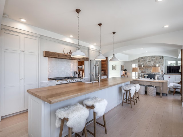 kitchen with a breakfast bar area, arched walkways, a sink, stove, and light wood-style floors