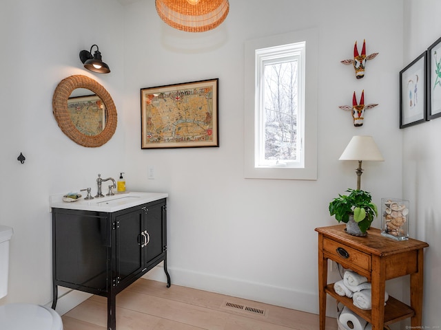 bathroom with vanity, wood finished floors, baseboards, visible vents, and toilet
