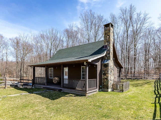 view of front facade featuring covered porch, roof with shingles, a front yard, and fence