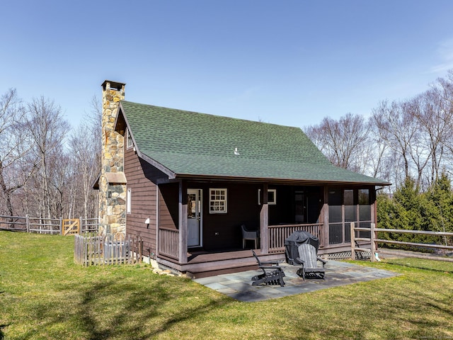 back of house featuring a shingled roof, fence, a chimney, a yard, and a sunroom