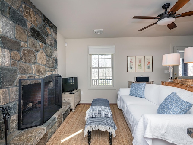 living room featuring visible vents, baseboards, ceiling fan, a fireplace, and wood finished floors