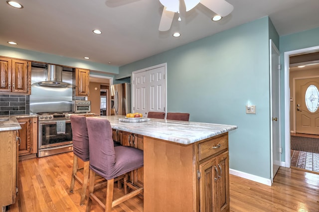 kitchen featuring a breakfast bar, stainless steel appliances, wall chimney exhaust hood, a kitchen island, and light wood-style floors