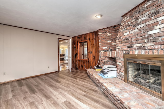 unfurnished living room featuring baseboards, a fireplace, wooden walls, and wood finished floors