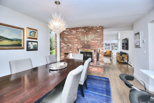 dining room featuring a brick fireplace, baseboard heating, an inviting chandelier, and wood finished floors