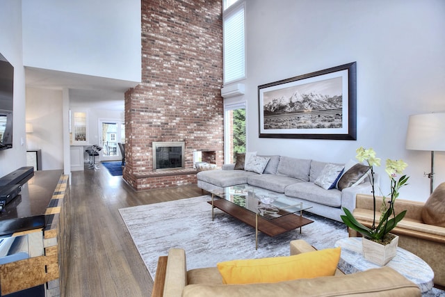 living room with a brick fireplace, a towering ceiling, and wood finished floors