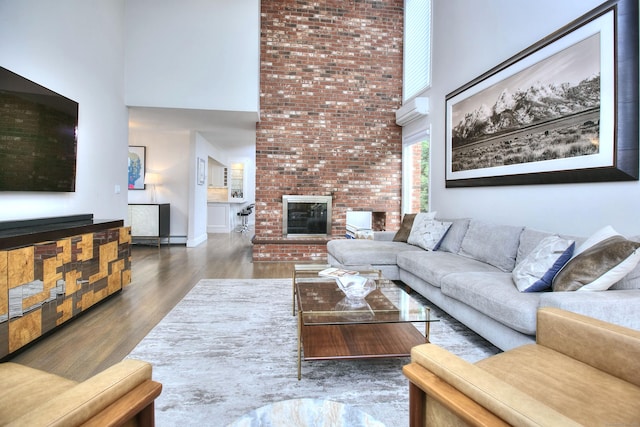 living area with a wall mounted air conditioner, a fireplace, a high ceiling, and wood finished floors