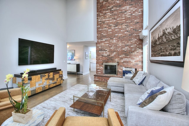 living room featuring a high ceiling, wood finished floors, baseboards, and a brick fireplace
