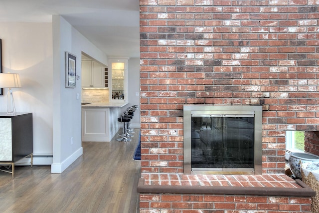 room details featuring baseboards, a brick fireplace, a baseboard radiator, wood finished floors, and decorative backsplash