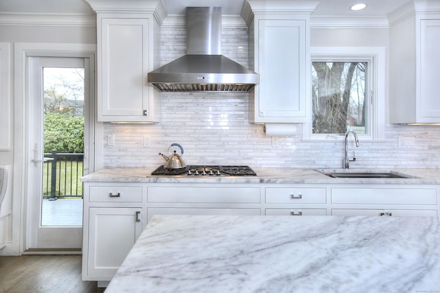 kitchen with a sink, backsplash, white cabinetry, and wall chimney exhaust hood