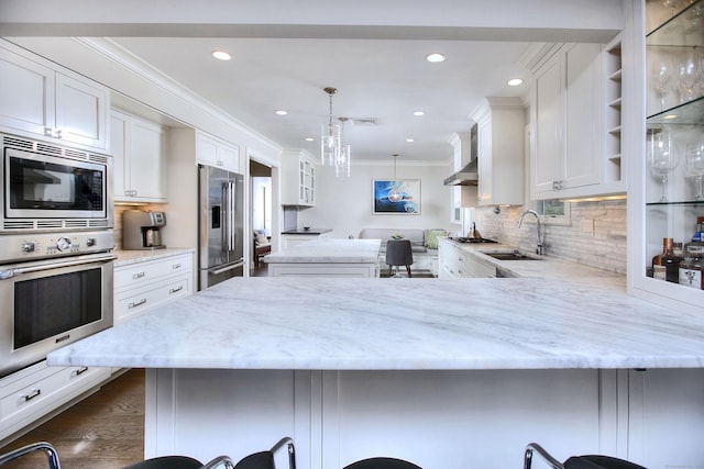 kitchen featuring white cabinets, a sink, appliances with stainless steel finishes, a peninsula, and crown molding