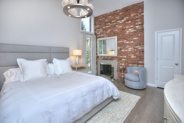 bedroom with wood finished floors, a fireplace, a notable chandelier, and a towering ceiling