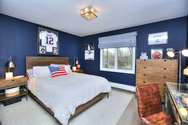 bedroom with a baseboard heating unit, baseboards, and wood finished floors