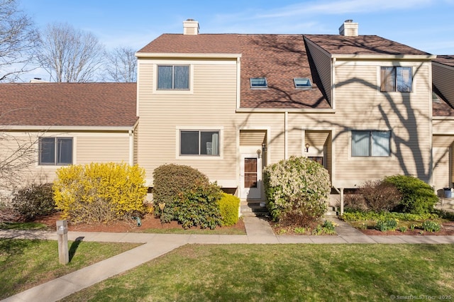 view of front of house with roof with shingles, a front lawn, and a chimney